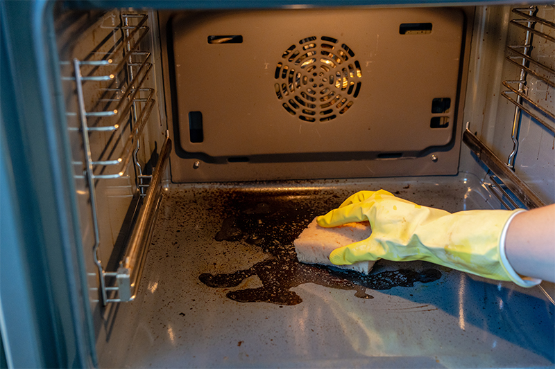 Professional Cleaner in a rubber glove cleaning dirty oven with sponge and cleaner. 